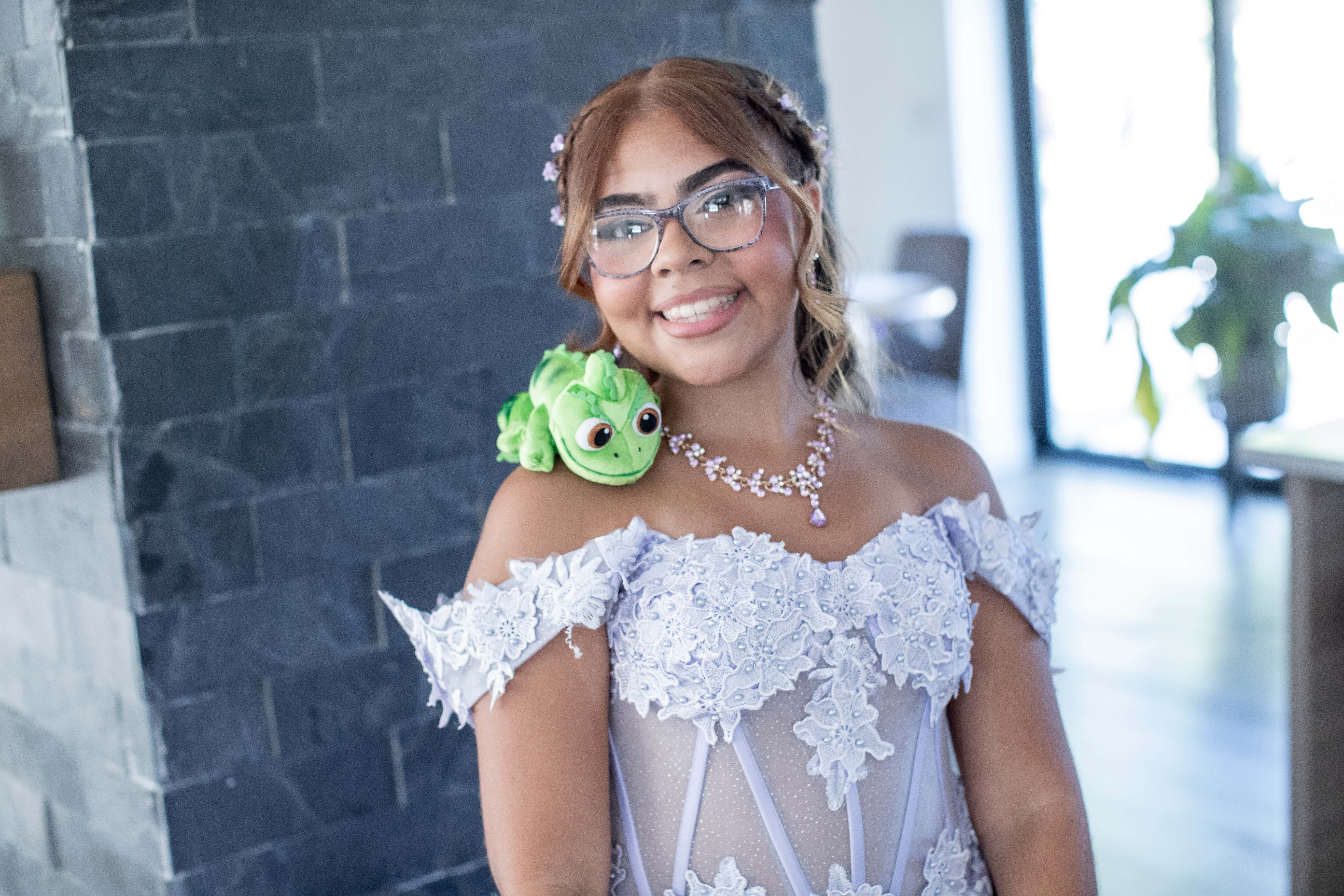 Young woman in a lavender lace gown smiling, with a small plush chameleon resting on her shoulder