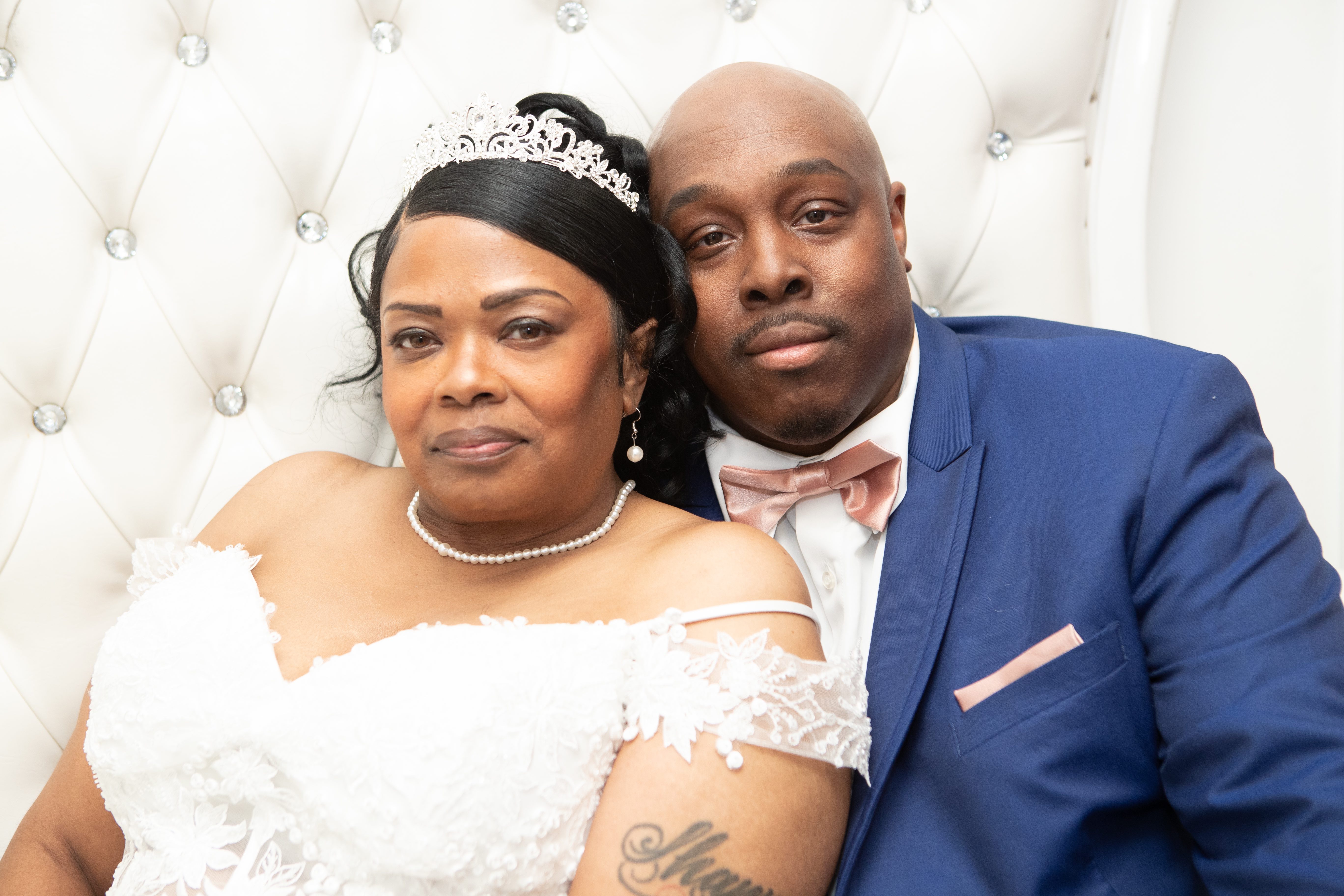 Bride in a tiara and pearls resting her head beside her groom in a navy suit and blush bow tie