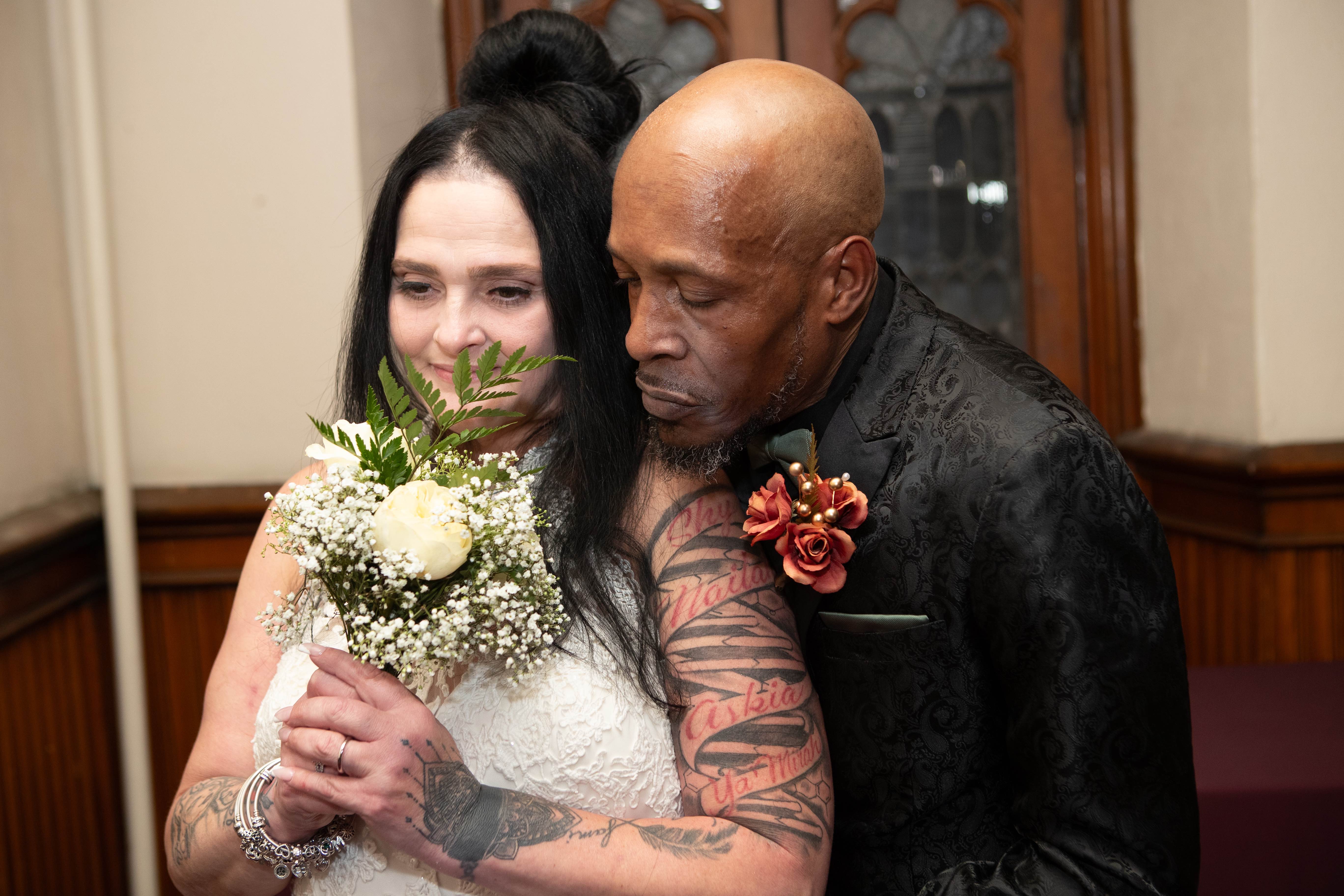 Groom holding his bride close as she holds a bouquet of white roses and baby's breath